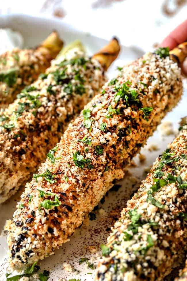 a hand picking up a piece of elote corn to eat