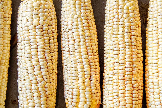 showing how to make elote by brushing chili powder olive oil over corn before grilling