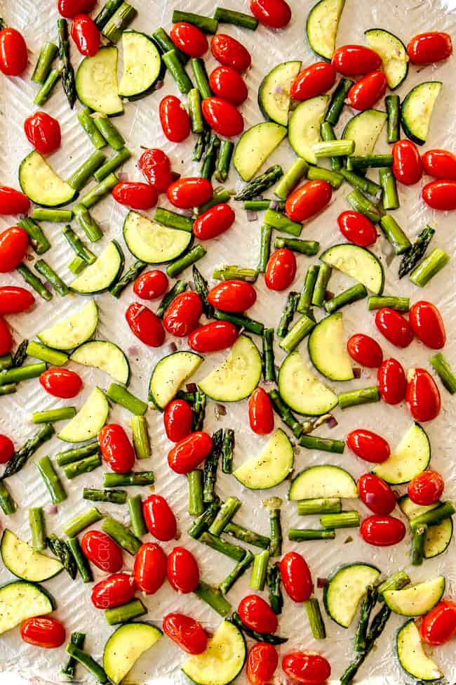 showing how to make lemon chicken pasta by adding tomatoes, zucchini and asparagus to a baking sheet