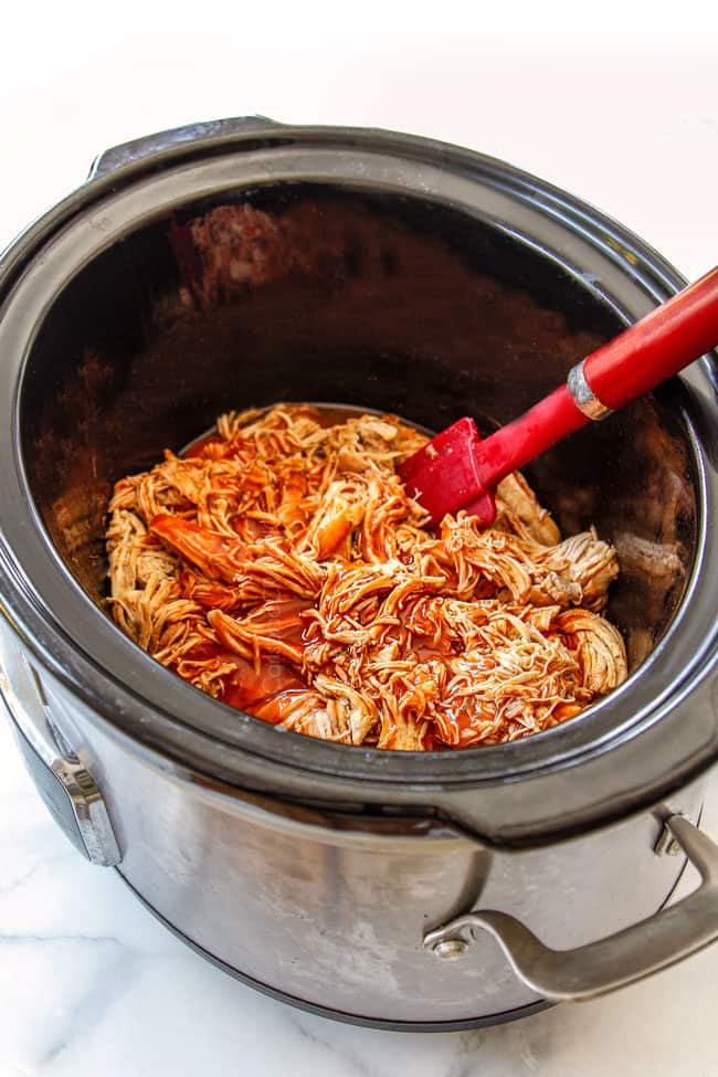 showing how to make slow cooker buffalo chicken by stirring hot sauce into shredded chicken