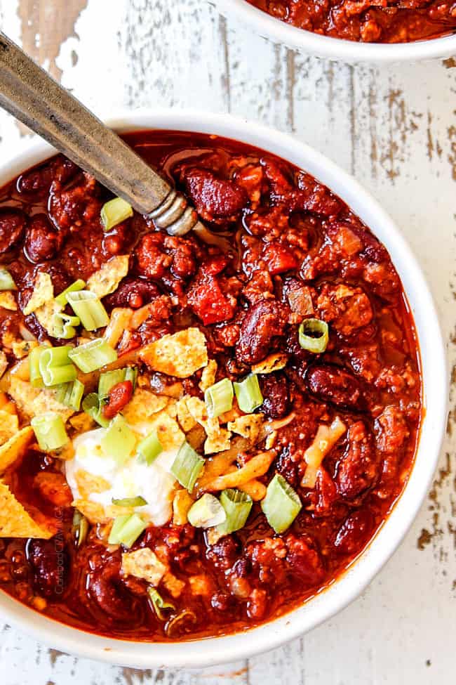 top view of crockpot chili recipe in a white bowl with cheese, green onions, sour cream