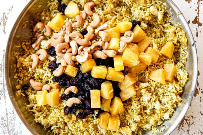 showing how to make pineapple fried rice by adding pineapple, cashews, craisins