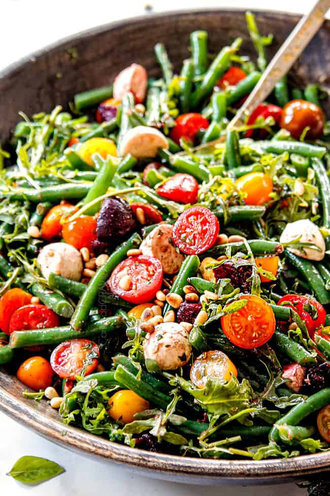 showing how to make cold green bean salad by adding green beans, tomatoes, beets to salad bowl