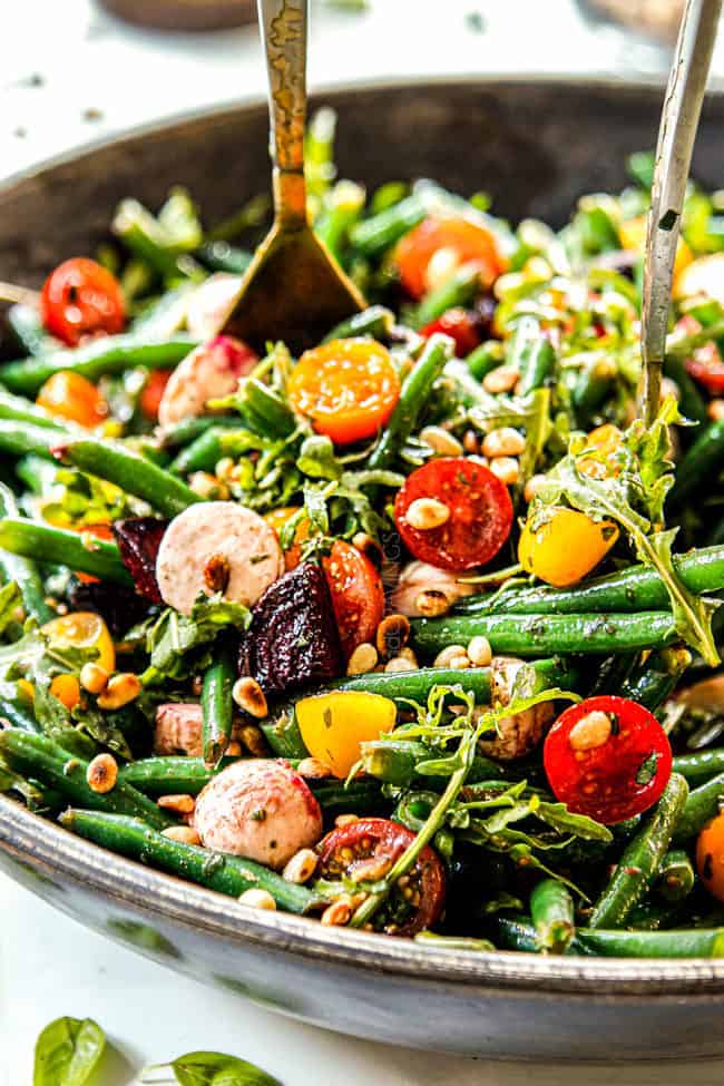 two tongs tossing fresh green bean salad