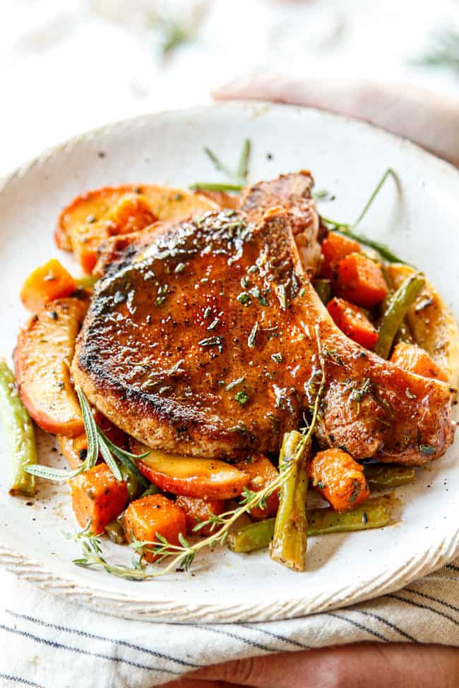 two hands holding a plate of brined pork chops with apples
