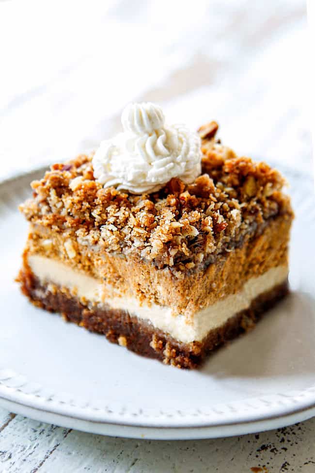 showing how to serve pumpkin cheesecake bars by placing a slice on a white plate with whipped cream