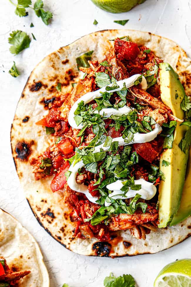 top view of showing how to make shredded chicken tacos by adding chicken, cilantro and avocados to tortilla