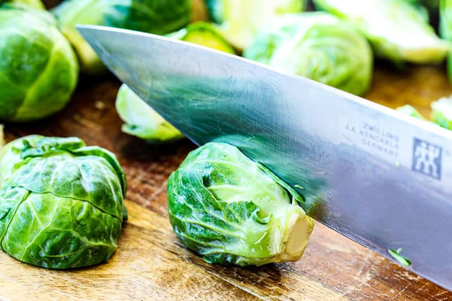 showing how to trim Brussels Sprouts on a cutting board by slicing sprout in half