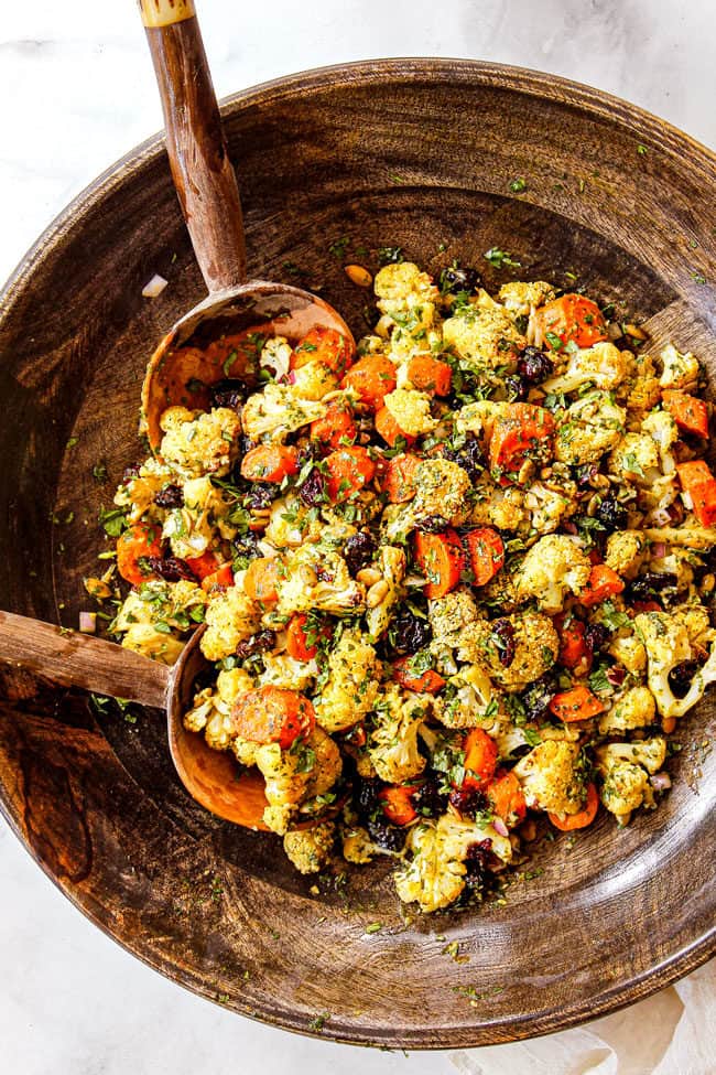 showing how to make Cauliflower Salad by tossing it in a large wooden bowl