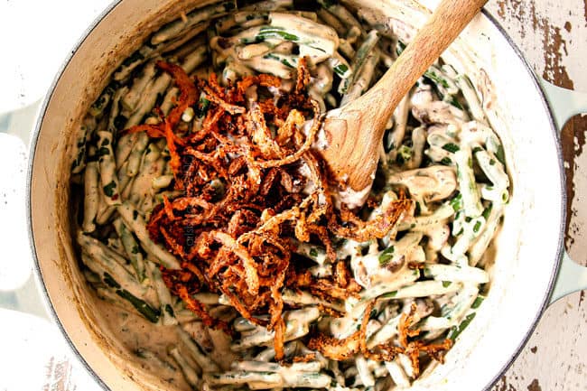 showing how to make best green bean casserole by adding fried onions to creamy green beans