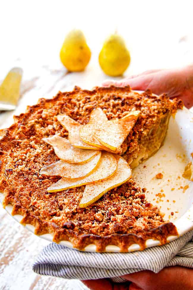 two hand serving pear pie with streusel topping