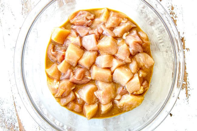 showing how to make Szechuan chicken by marinating chicken in a glass bowl with soy sauce, rice wine, sesame oil and cornstarach