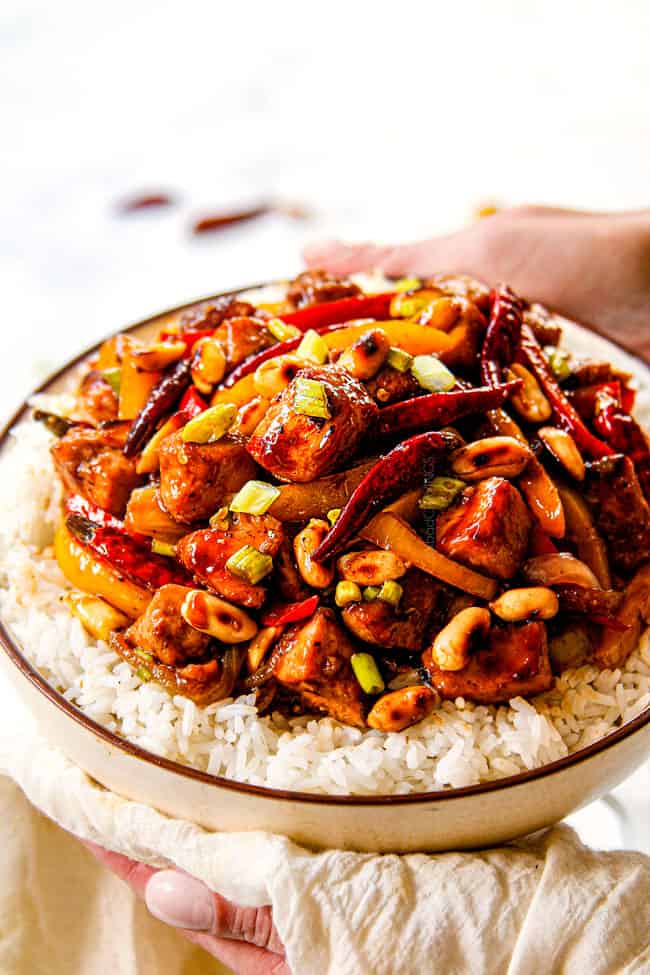 two hands holding a bowl of chicken szechuan style
