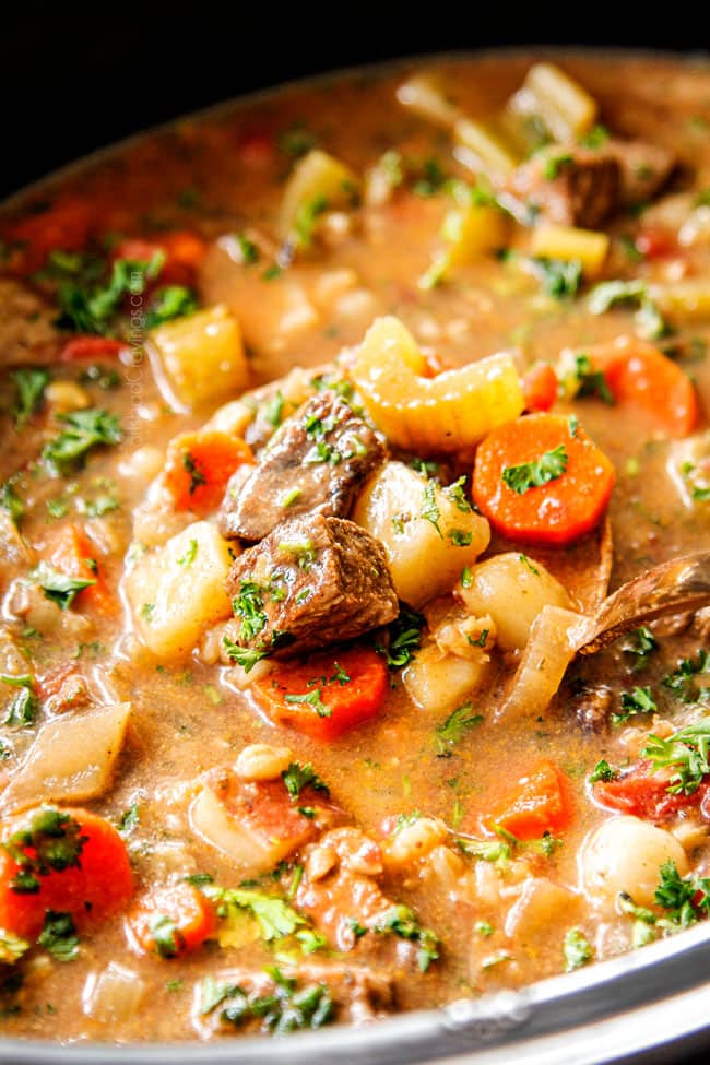 showing how to serve slow cooker beef barley soup by scooping up a spoonful of soup in a ladle
