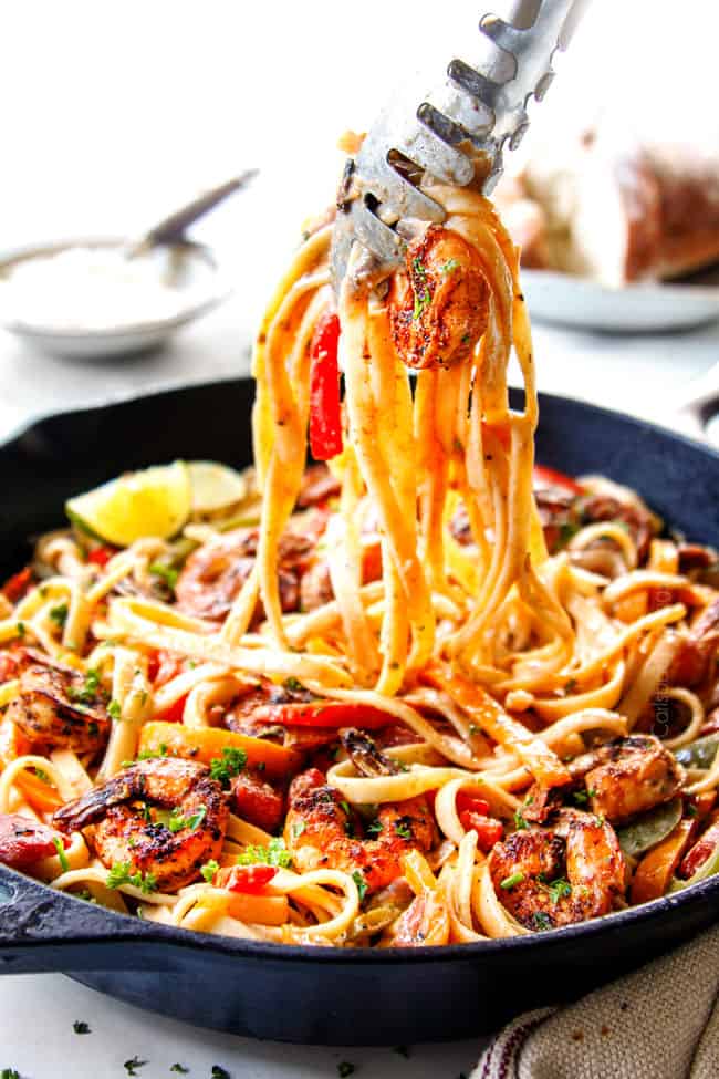 showing how to serve creamy Cajun Shrimp Pasta recipe by picking up shrimp and fettuccine with tongs