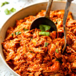 two tongs scooping up chicken tinga to serve