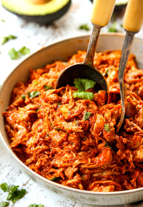 two tongs scooping up chicken tinga to serve