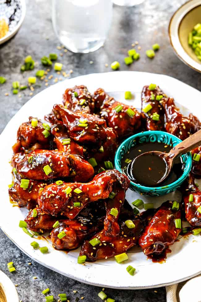 showing how to serve Korean Chicken Wings by adding to a platter and garnishing with sesame seeds and green onions