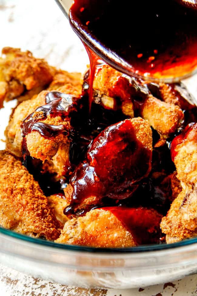 showing how to make Korean Chicken Wings recipe by adding baked wings to a bowl then pouring Korean BBQ Sauce with gochujang all over the wings