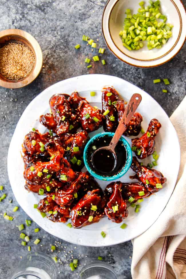 top view of Korean Chicken Wings recipe on a white platter with green onions and Korean BBQ Sauce