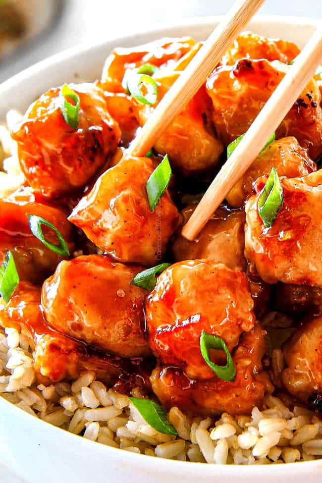 showing how to eat homemade orange chicken recipe by picking up a piece of chicken with chopsticks