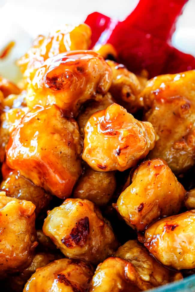 showing how to make orange chicken by stirring baked breaded chicken until evenly coated in the sauce