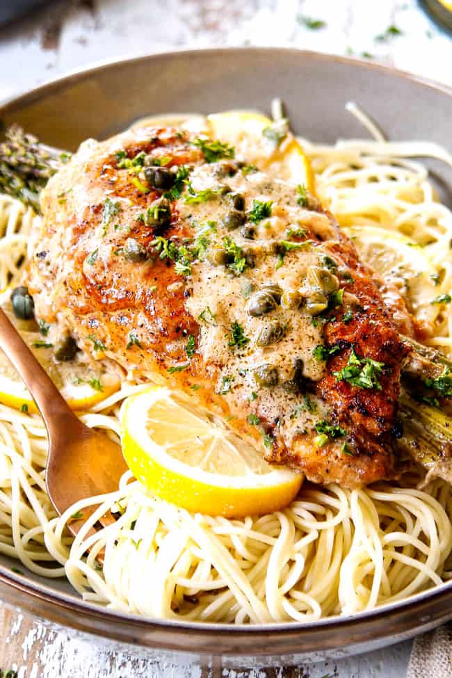 up close of a piece of chicken piccata on a bowl of linguine pasta showing what to serve with chicken piccata