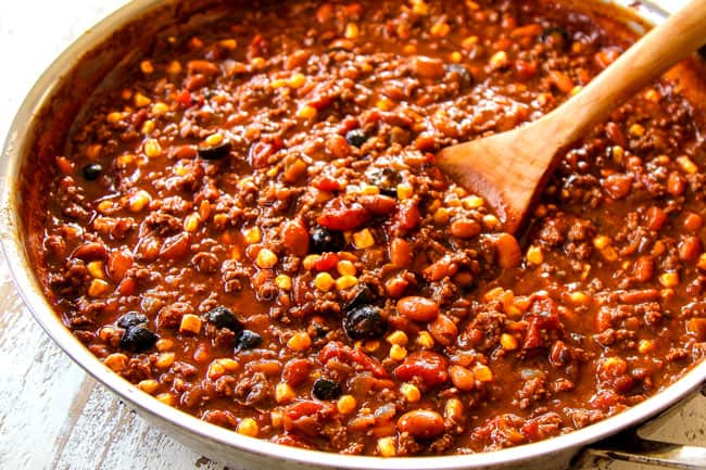 showing how to make Mexican Lasagna recipe by warming beans,corn and olives in a large skillet with the beef and sauce