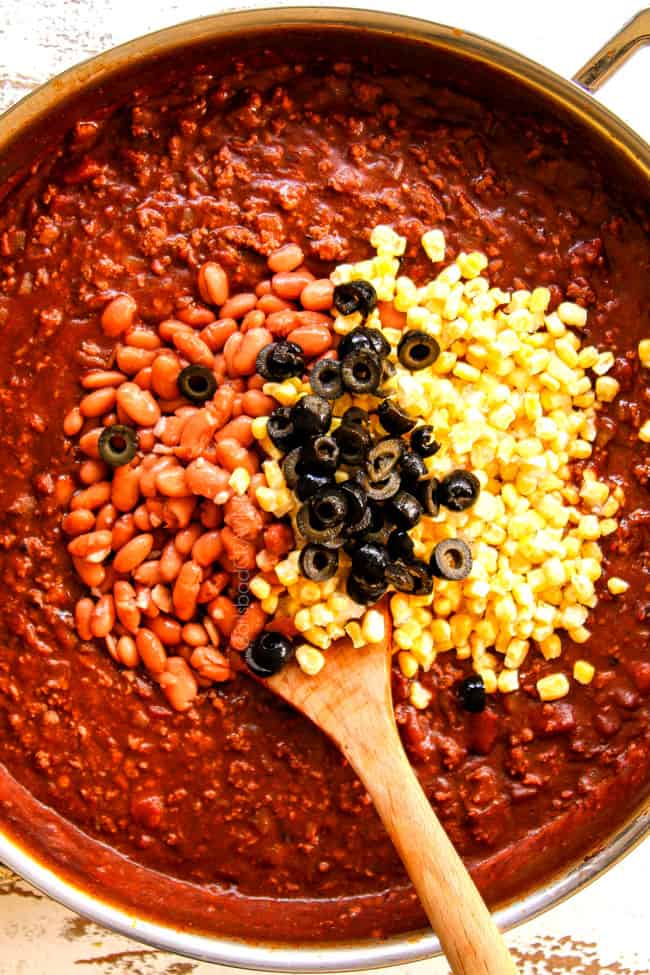 showing how to make Mexican Lasagna recipe by adding pinto beans, black olives and corn to saucy beef mixture