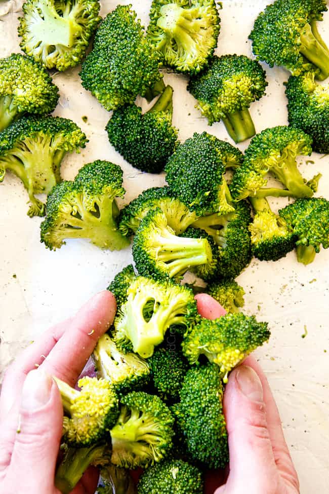 showing how to make salmon pasta by seasoning broccoli with salt, pepper and olive oil before adding next to salmon