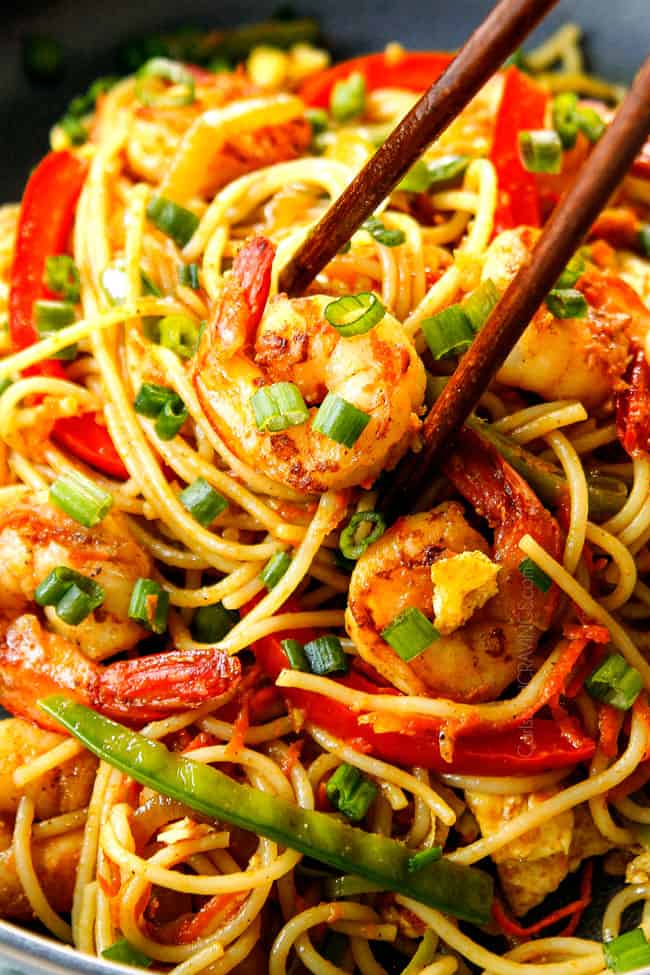 up close of showing how to eat Singapore Noodles recipe by picking up a piece of shrimp and noodles with chopsticks