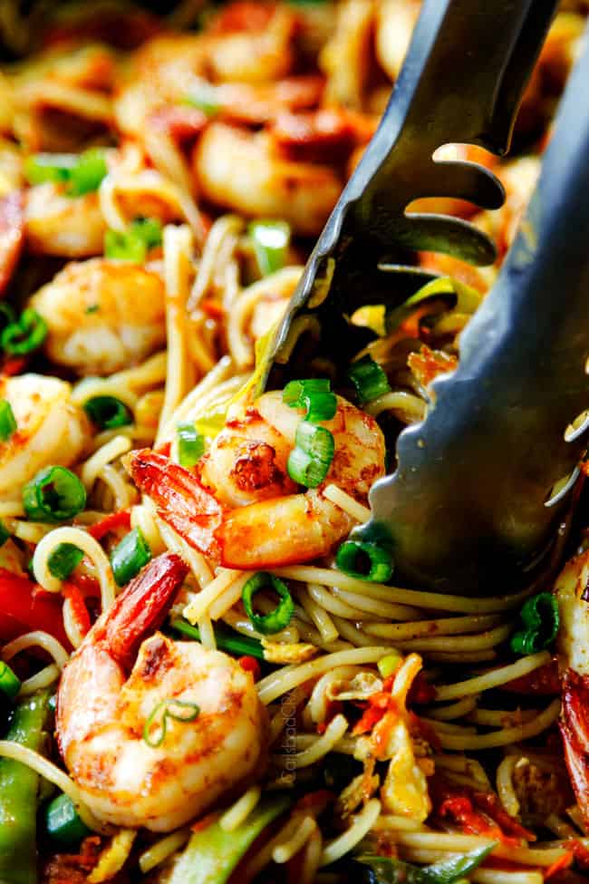 up close of picking up Singapore noodles garnished with green onions with tongs