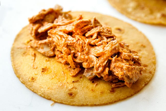 showing how to make chicken enchilada recipe by adding chicken filling to the center of corn tortillas and rolling up