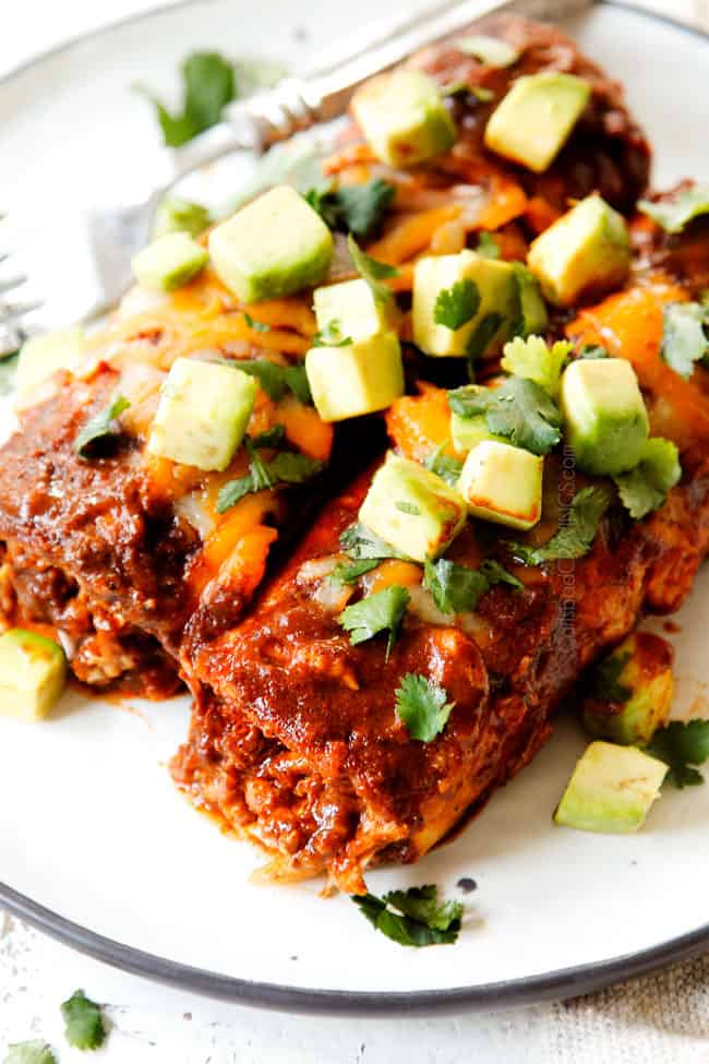 showing how to serve chicken enchilada recipe by adding two red chicken enchiladas to a plate and garnishing with sour cream