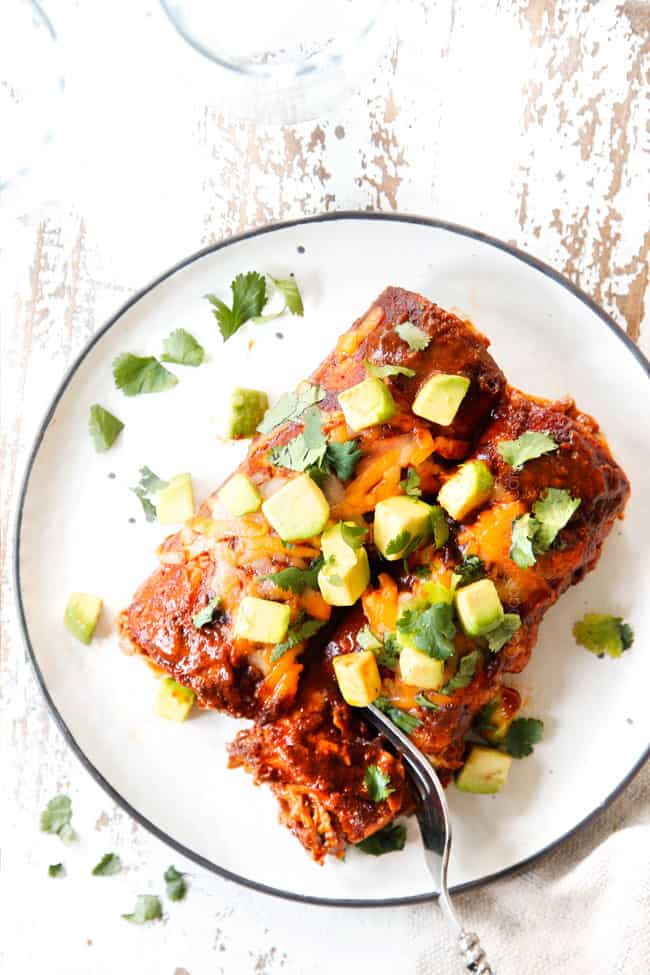 top view of two easy chicken enchiladas on a plate with a fork taking a bite out of one of the enchiladas