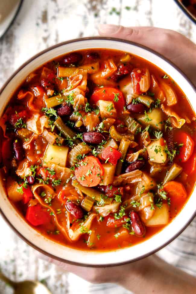 showing how to make best Cabbage Soup recipe by adding red pepper flakes to a bowl of soup.