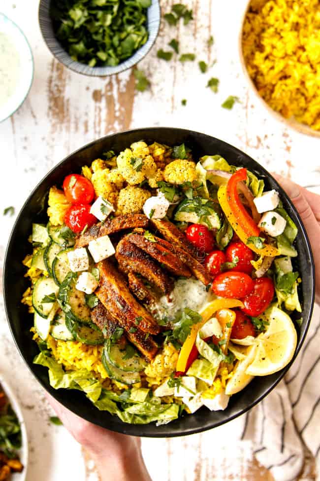 showing to make chicken shawarma recipe by adding chicken to rice, lettuce, tomatoes and bells to make salad bowl