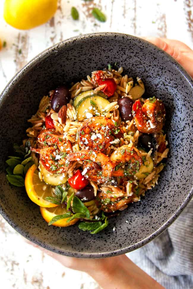 two hands holding a bowl of lemon garlic shrimp recipe with pasta