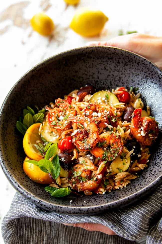 showing how to serve shrimp recipe with two hand holding a black bowl of lemon garlic shrimp with pasta garnished with mint