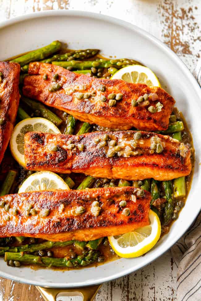 showing how to make lemon salmon and asparagus recipe by by spooning piccata sauce over fish