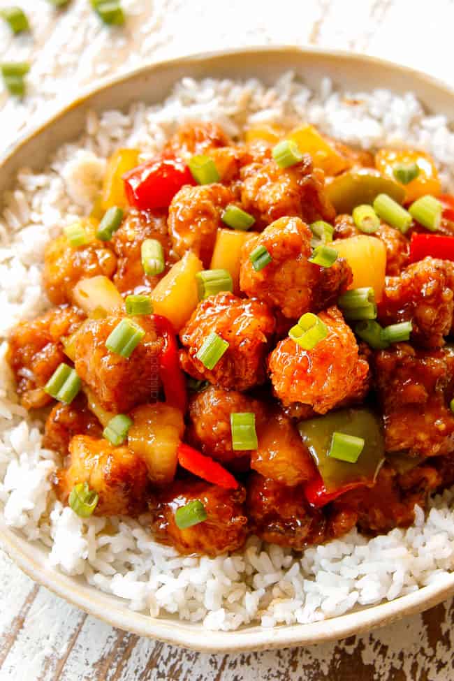 showing how to serve Chinese Sweet and Sour Chicken by adding to a bowl of rice and garnishing with green onions