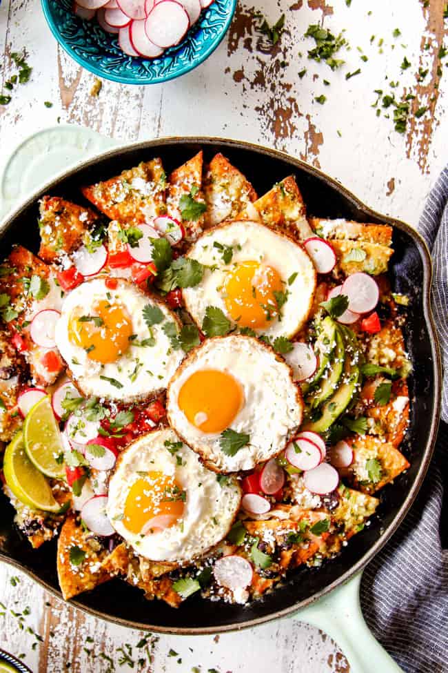 top view of a skillet showing how to garnish Chilaquiles recipe by adding Fried Eggs, avocados, queso fresco, and cilantro