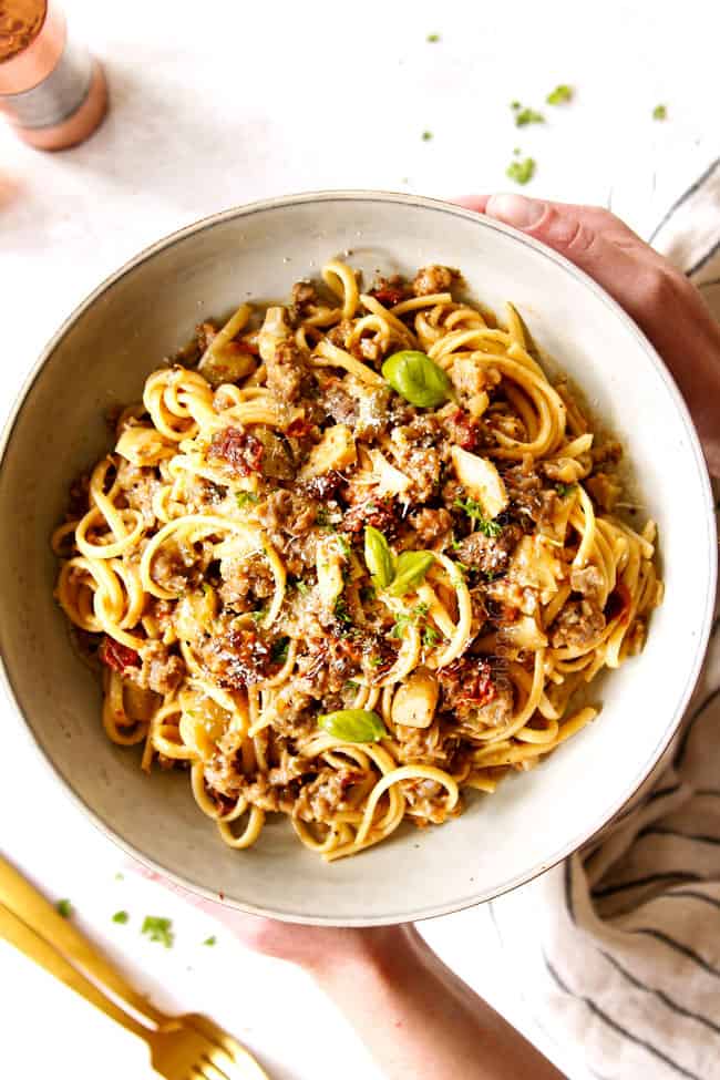 showing how to serve linguine noodles with two hands holding a bowl of linguine garnished with fresh basil and Parmesan