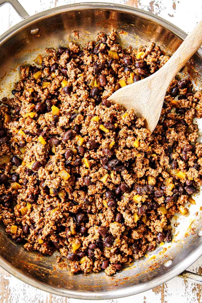 showing how to make beef enchilada recipe by stirring black beans and enchilada sauce with ground beef