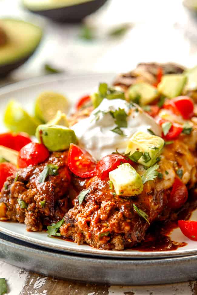 showing how to serve beef enchilada recipe adding two enchiladas to a plate and topping with sour cream, cilantro and tomatoes