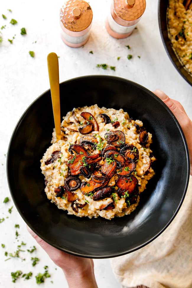 showing how to serve mushroom risotto recipe by adding to a small black bowl and garnishing with parsley