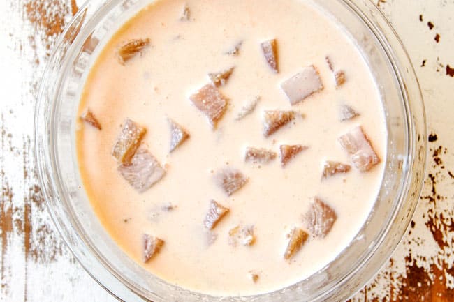 showing how make KFC Popcorn Chicken by marinating chicken in buttermilk in a glass bowl