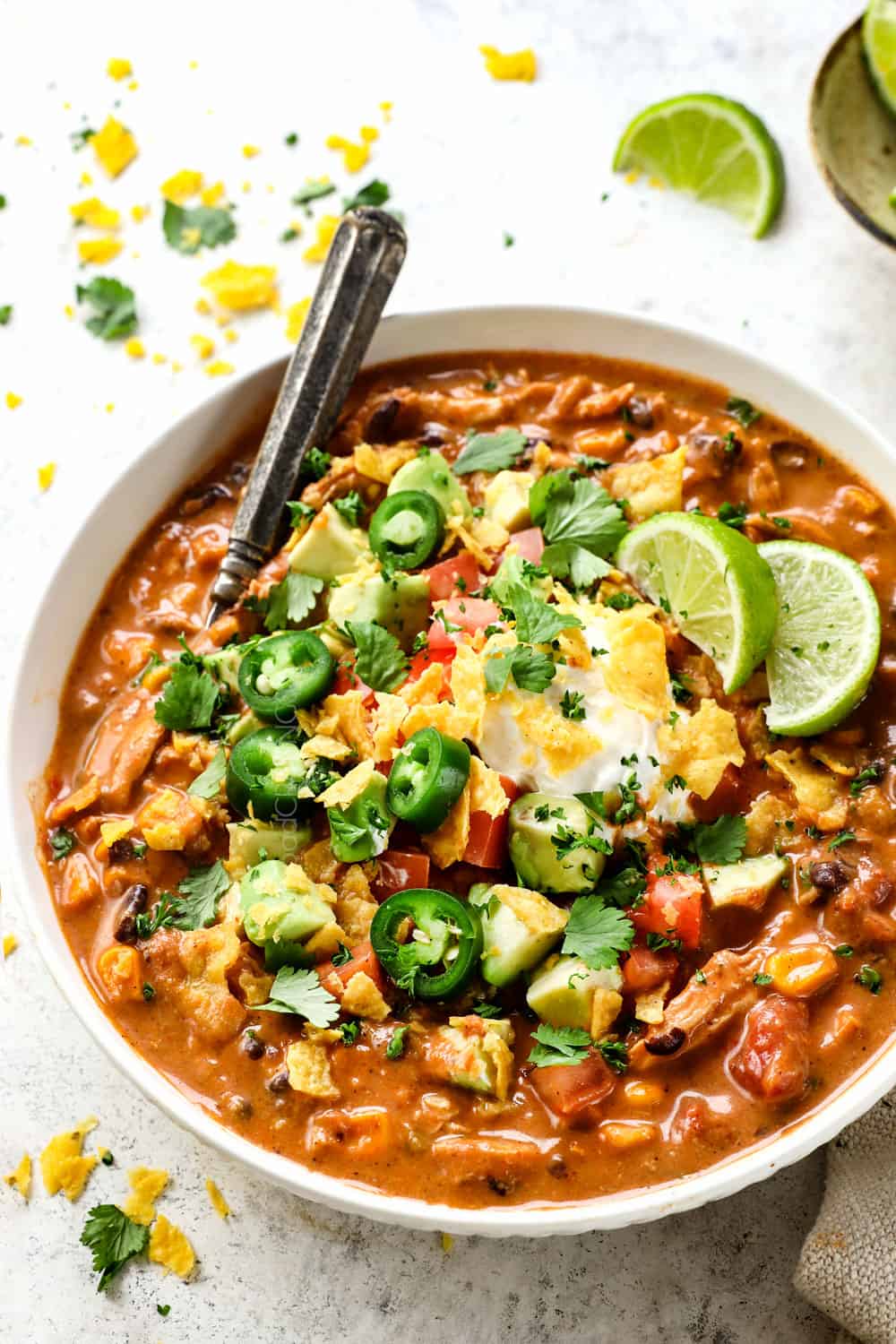a bowl of creamy chicken enchilada soup garnished with sour cream, cilantro chips and avocados