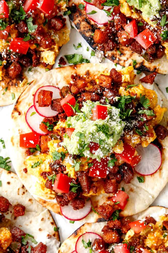 top view of breakfast tacos lined on a white tray layered with chorizo, potatoes and scrambled eggs