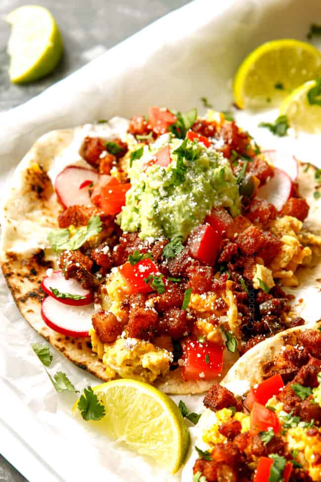 up close of breakfast tacos showing what to add to tortillas - scrambled eggs, chorzio and potatoes topped with avocados and tomatoes.